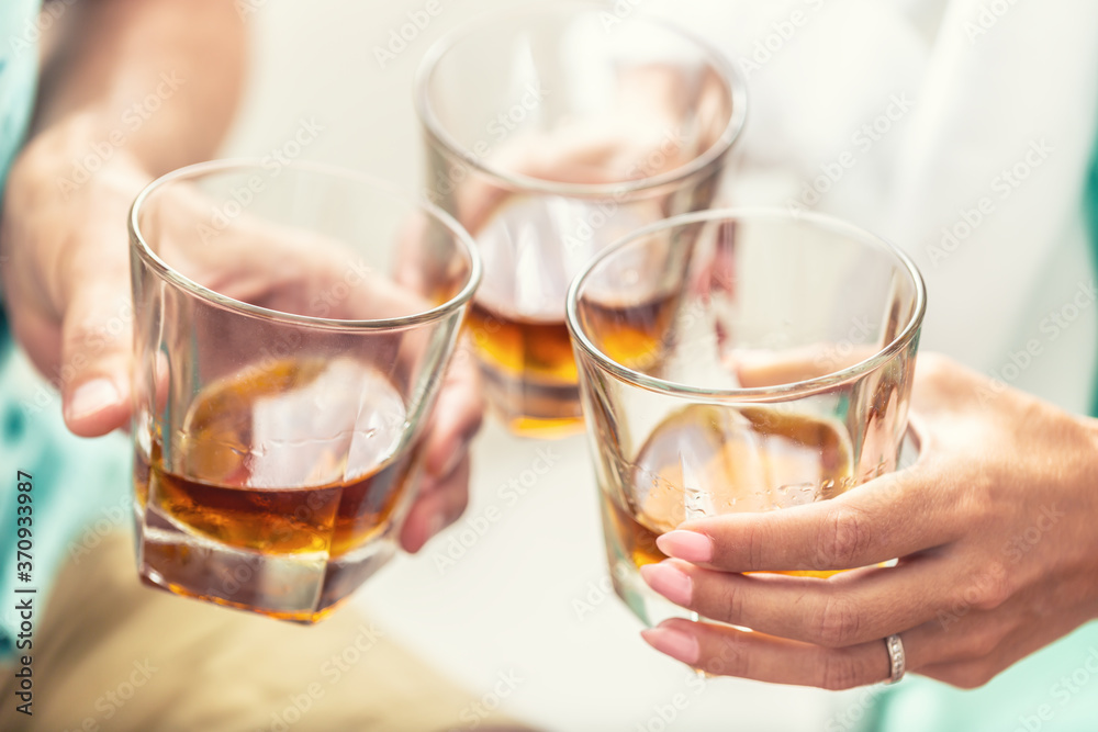 Group of friends toasting with glasses of whiskey brandy or rum indoors - closeup Group of friends toasting with glasses of whiskey brandy or rum indoors - closeup