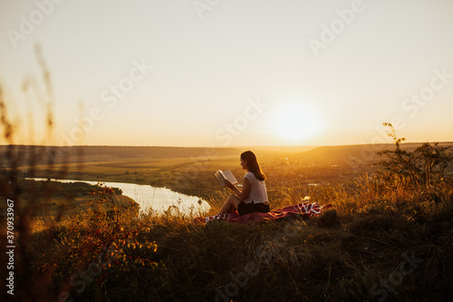 Calm girl reading a book on hill with perfect landscape  enjoying time on holiday. She read book in quiet nature.