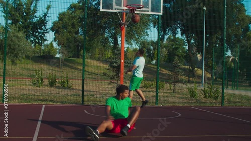 Athletic sporty mixed race street basketball player driving to the hoop with ball, committing offensive foul of charging against opposing defender while playing basketball game on outdoor urban court.