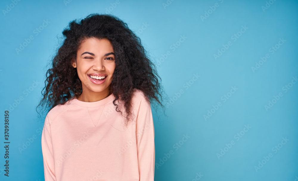 Fototapeta premium Winking cute African-American woman with curly hair on a blue background.