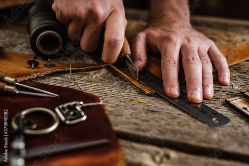 Close up of a shoemaker or artisan worker hands. Leather craft tools on old wood table. Leather craft workshop.