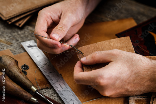 Close up of a shoemaker or artisan worker hands. Leather craft tools on old wood table. Leather craft workshop.