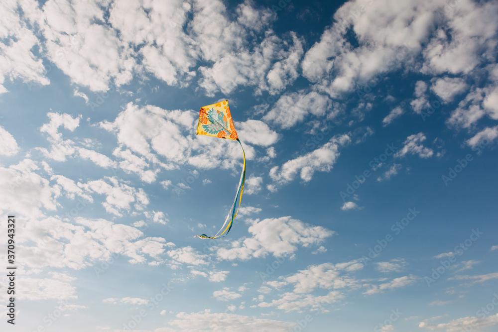 Colorful kite flying on blue sky background with white clouds. Stock