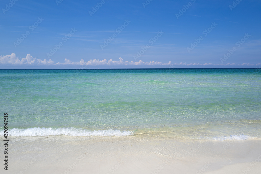 Soft blue ocean wave on clean sandy beach.