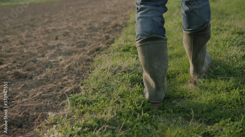 Follow to male farmer feet in boots walking through the small green sprouts on the field agriculture green examine farmer field ground land nature walk worker boots close up cultivate farm industry