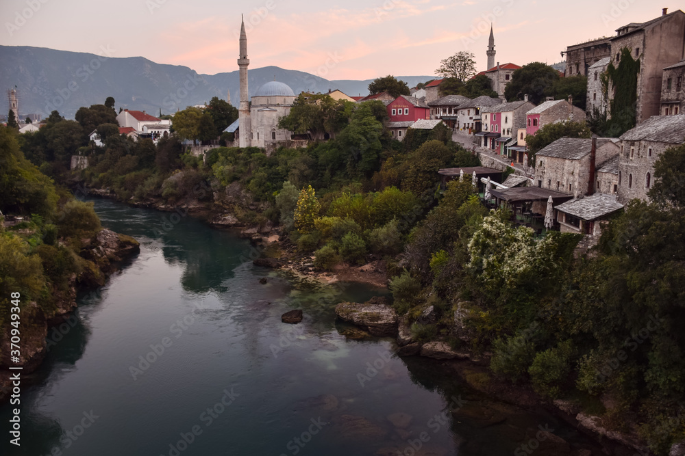 Mostar village with mosque and houses reflected on the water of river during sunset time