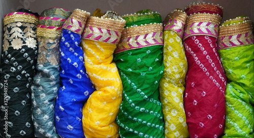 Traditional Rajasthan dress materials is neatly stacked for sale in a cloth merchant shop in India. Colorful fabric street stall. Bandhej or Bandhani widely used in Rajasthan
