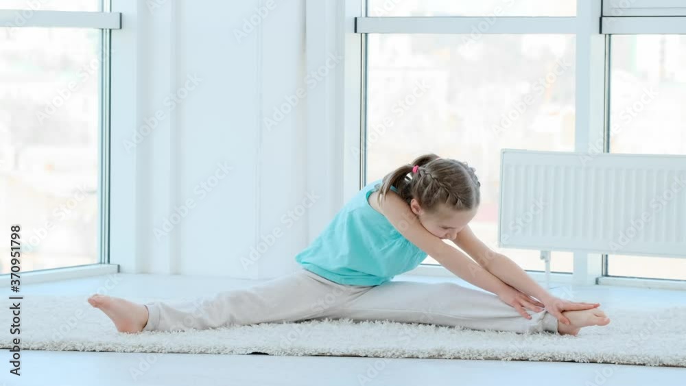 Pretty little girl doing physical exercises alone in light room