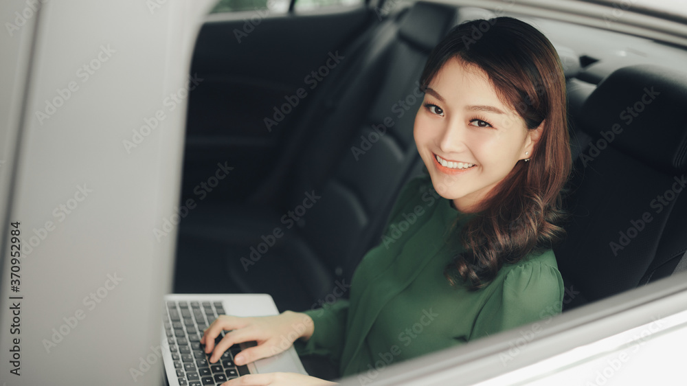 Beautiful businesswoman using laptop while sitting on a backseat of a car. Beautiful businesswoman using laptop while sitting on a backseat of a car.