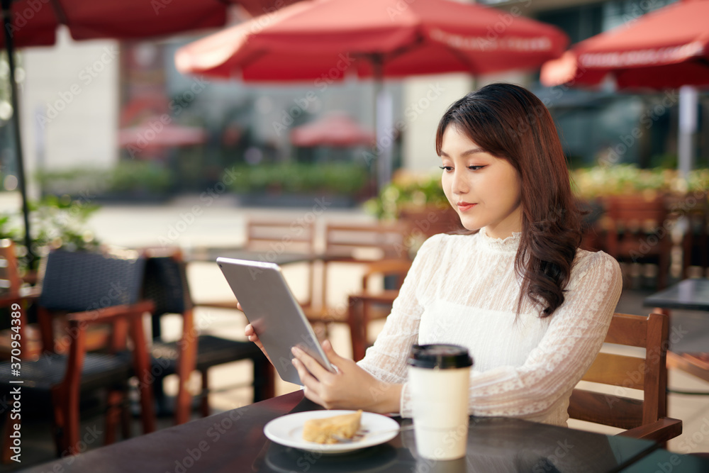 Young and beautiful Asian woman using her tablet PC while sitting at outdoor coffee shop in the urban city