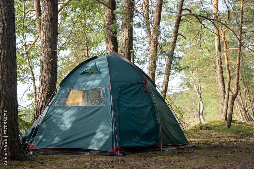 A large tourist tent is set up on the campground in a beautiful forest by the lake. Camping with a tent. Self-isolation in the forest during the COVID-19 quarantine.