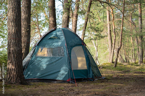 A large tourist tent is set up on the campground in a beautiful forest by the lake. Camping with a tent. Self-isolation in the forest during the COVID-19 quarantine.
