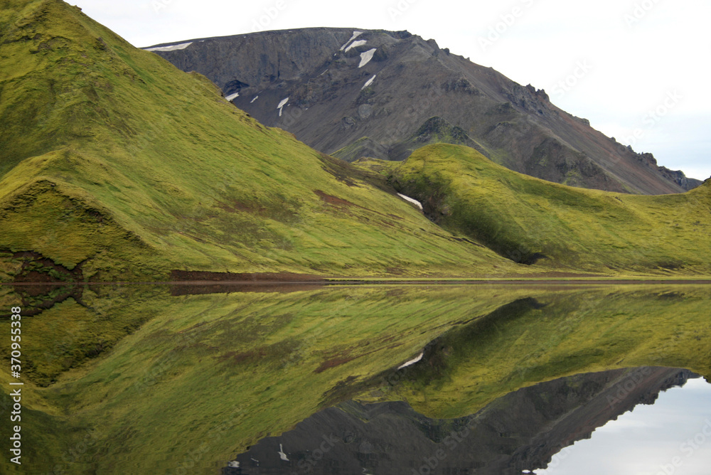 Green hill with sort of moss, reflection in the backwater in a river in Iceland Green hill with sort of moss, reflection in the backwater in a river in Iceland
