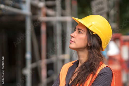 Profile portrait of an attractive female factory worker wearing a yellow protective helmet and looking aside