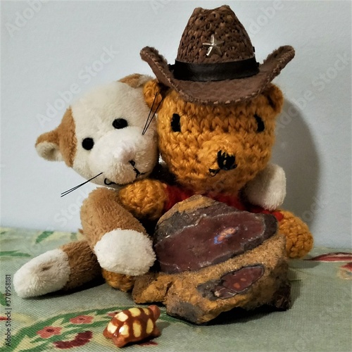 Tiny crocheted teddy bear in cowboy hat being hugged by tiny cat toy,  with an opalised rock and miniature clay tortoise in the foreground. photo