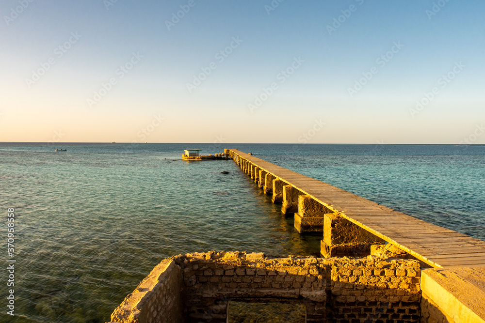 Old wooden pier (jetty) of the Sanganeb Reef Lighthouse near Port Sudan, on  the Red Sea, in Sanganeb National Park, with endless horizon sea view  during golden hour sunset. Stock Photo