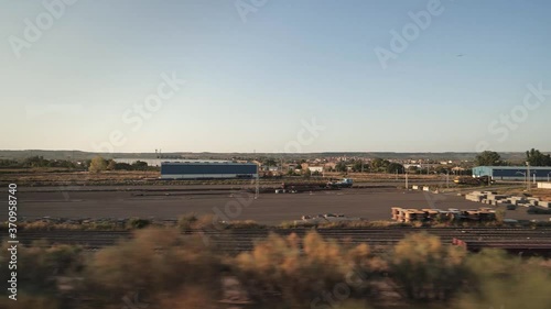 View to a landscape from the window of the moving train at the sunset. Industrial area with warehouse buildings and barns