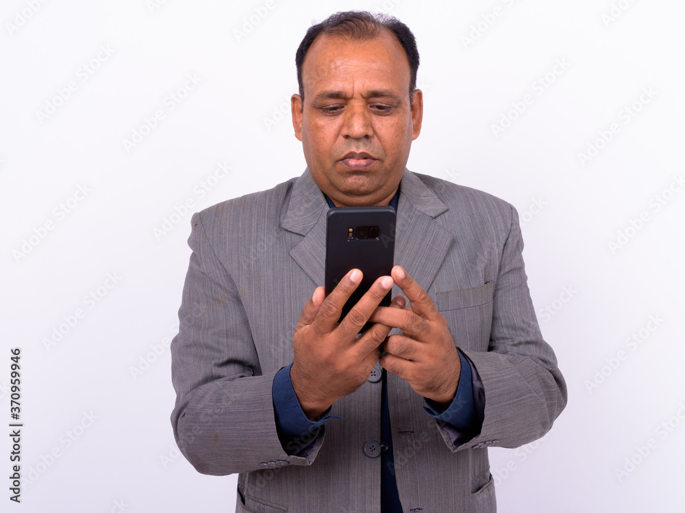 Portrait of mature overweight Indian businessman in suit using phone Portrait of mature overweight Indian businessman in suit using phone