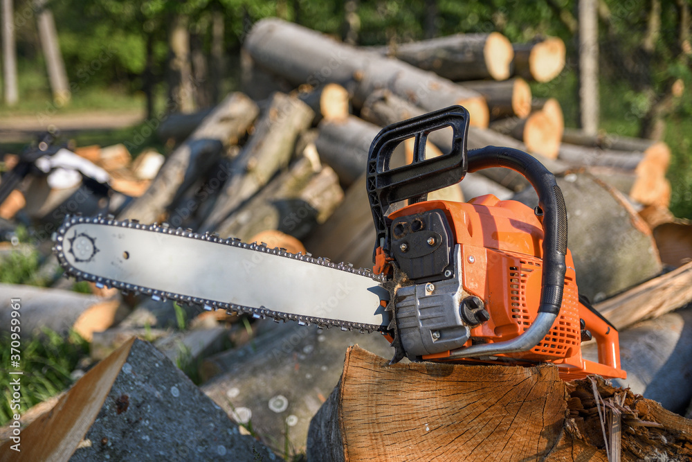 Chainsaw that stands on a heap of firewood in the yard on a background of firewood and trees cut by a chainsaw