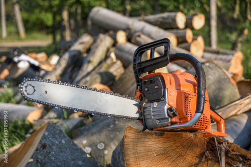 Chainsaw that stands on a heap of firewood in the yard on a background of firewood and trees cut by a chainsaw photo