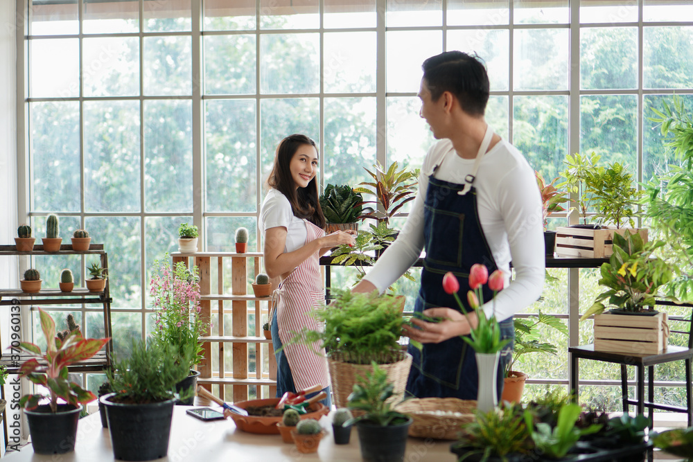 Happy young Asian couple wearing apron uniforms gardening, watering and take care of their plants together at home