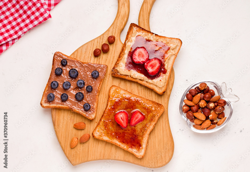 Peanut butter and jelly sandwich on a wooden board next to nuts