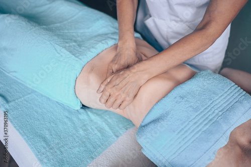 Young unrecognizable woman lying on massage table and enjoying therapeutic massage. Body care, losing weight concept. Hands masseur massage therapist doing anti-cellulite massage in spa clinic.