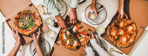 Pizza party for friends or family. Flat-lay of pizzas in boxes, lemon drinks and peoples hands cutting pizzas over white table background, top view. Fast food, comfort food, Italian cuisine concept