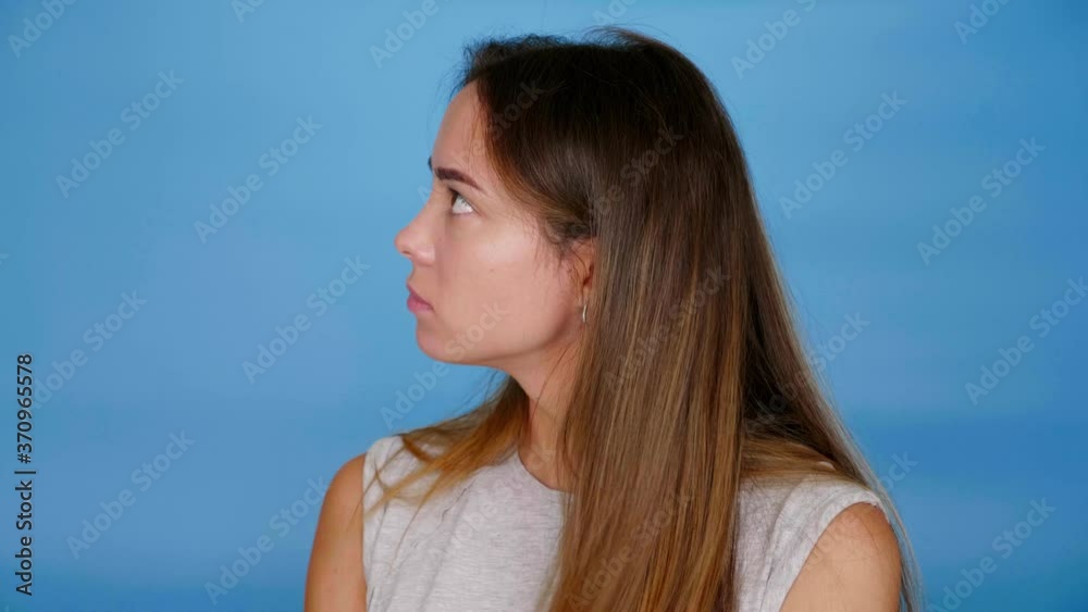 Beautiful woman in gray t-shirt looks around on blue background with copy space. 4K slow motion footage Beautiful woman in gray t-shirt looks around on blue background with copy space. 4K slow motion footage