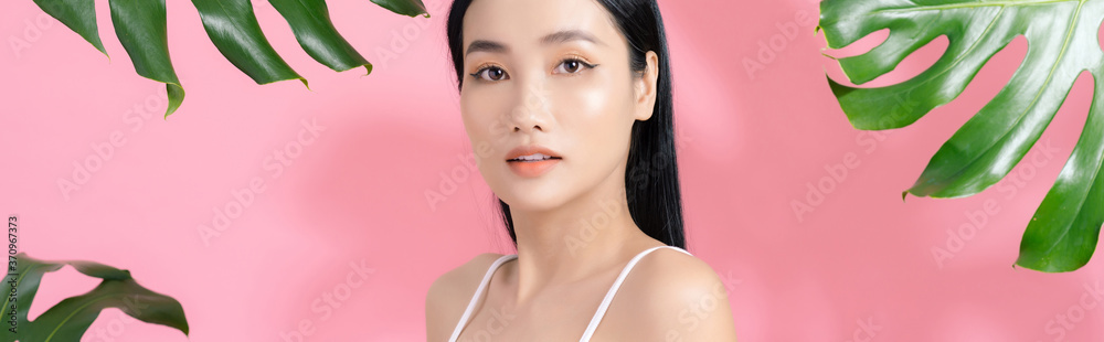 Natural cosmetics. Sensual Asian woman against tropical leaves, looking at camera on pink background