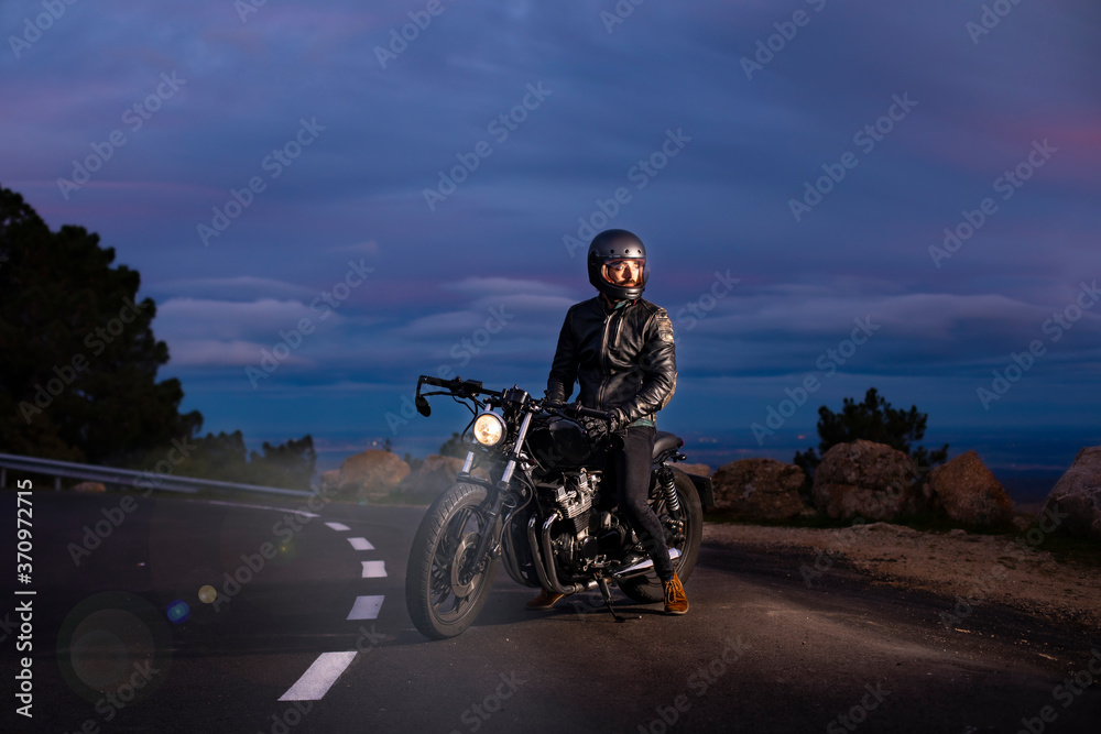 Rider with black cuscom motorcycle on the road at dusk