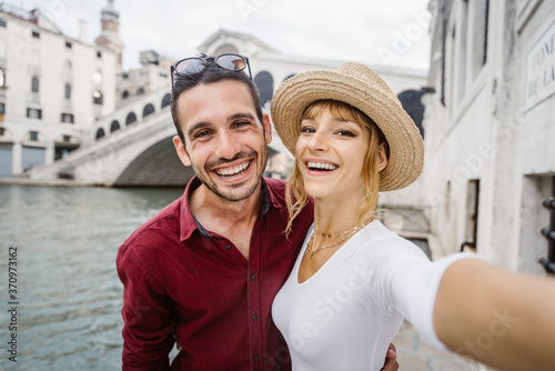Young couple taking a selfie portrait in front of Rialto Bridge in Venice, Italy.