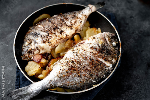 fried dorado fish and potatoes in a frying pan on a stone background photo