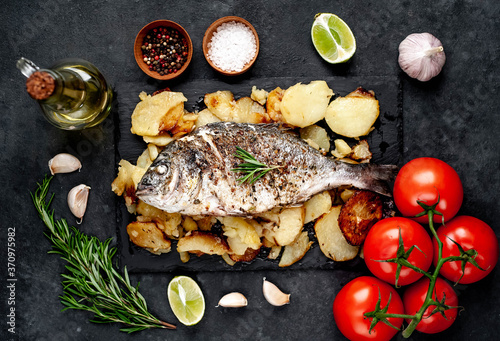 fried dorado fish and potatoes with ingredients on stone background photo