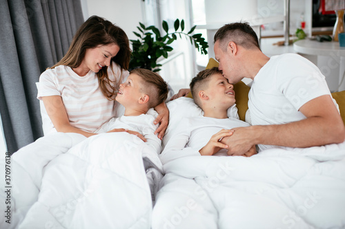 Young family enjoying in bed. Happy parents with sons relaxing in bed..