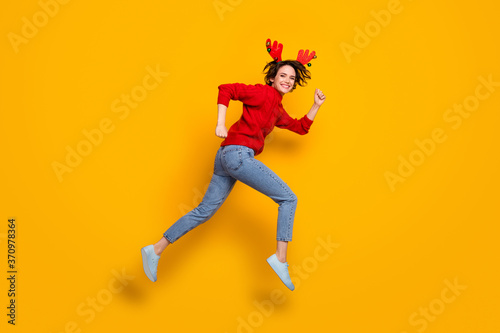 Full size profile photo of pretty funny lady jump high up rushing newyear sale shopping center wear headband x-mas horns red knitted sweater jeans shoes isolated yellow color background