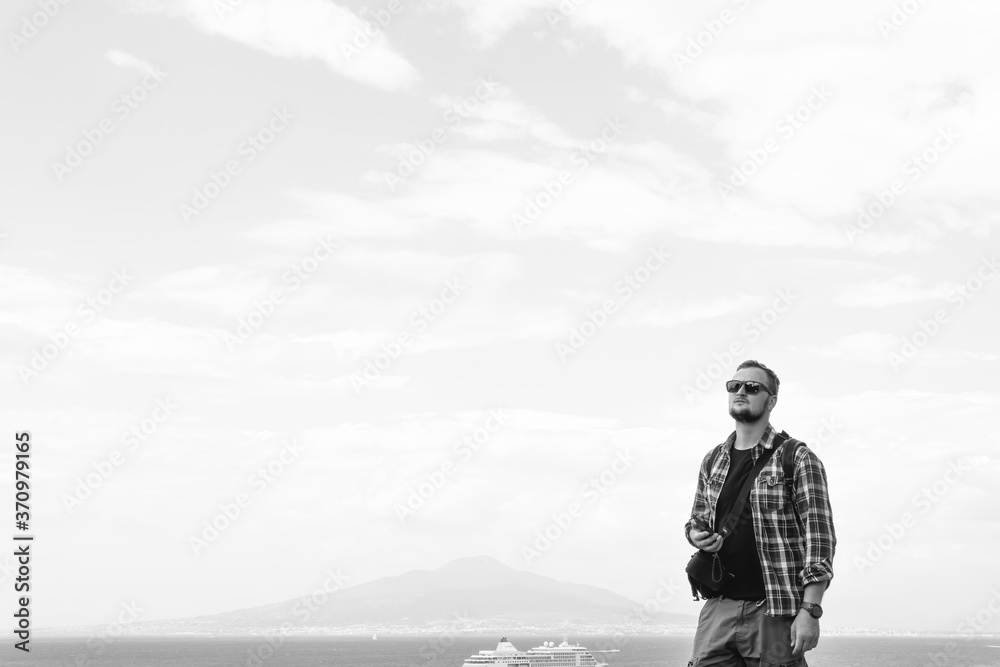 Young man with backpack standing with view on vulcano Vesuvius sea, ocean liner ship water craft. Travel and vacation concept. Dramatic black and white