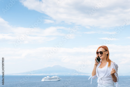 Pretty girl Emotions, shares his impressions by phone. Joy and happiness. Sea and horizon. Vacation and travel concept. Communication on a mobile network. Vesuvius volcano and ocean liner. Copy space © Sergey