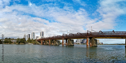 Beautiful panoramic view of a railway bridge across a river on a sunny day with deep blue sky and light clouds, Parramatta river, Meadowbank, Sydney, New South Wales, Australia
