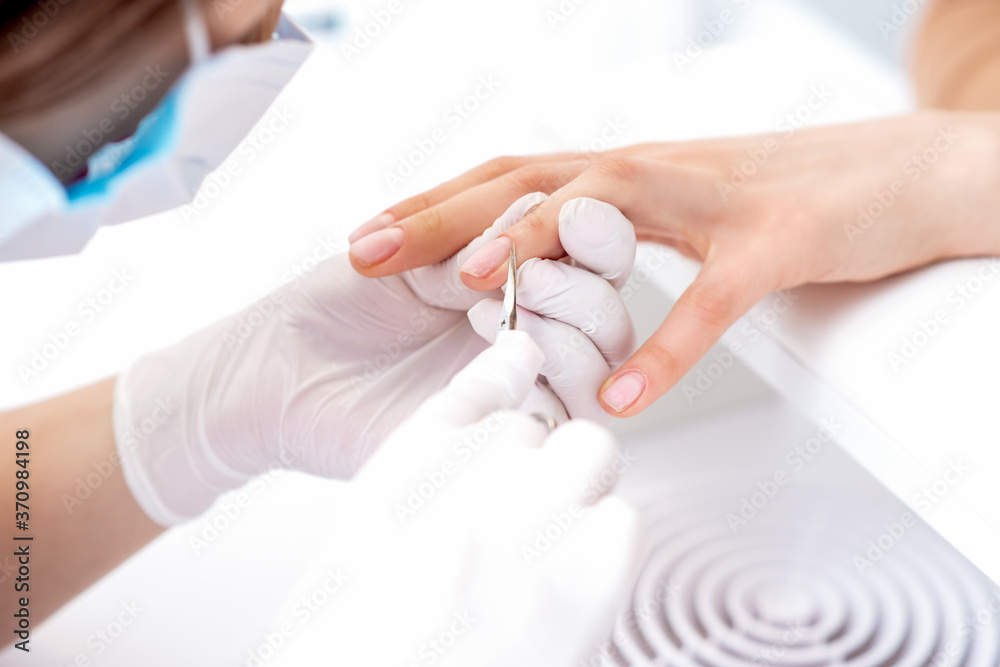 Naklejka premium Close up of manicurist using manicure scissors to remove cuticle of female nails in manicure salon