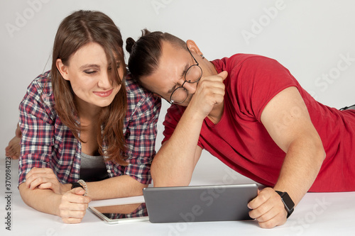 Young couple watching media content online in a tablet lying down and laughing. Wearing casual, stylish and funny. Common internet surfing concept, white background, copy space.