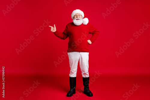 Full size photo old retired pensioner man point finger copyspace indicate x-mas fairy holly jolly ads wear santa headwear jumper trousers black boots isolated bright shine color background
