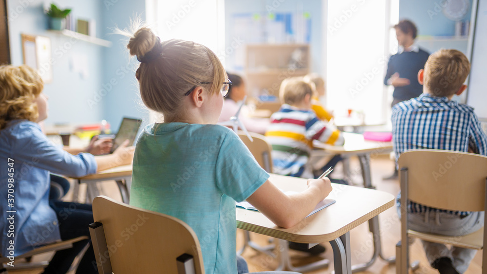 Elementary School Science Class: Cute Little Girl is Listening to a Teacher and Making Notes. Physics Teacher Explains Lesson to a Diverse Class full of Smart Kids. Over the Shoulder Shot. - obrazy, fototapety, plakaty 