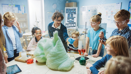 Elementary School Science / Chemistry Classroom: Enthusiastic Teacher Shows Funny Chemical Reaction Experiment to Group of Children. Mixing Chemicals in Beaker so they Shoot Foam (Elephant Toothpaste)