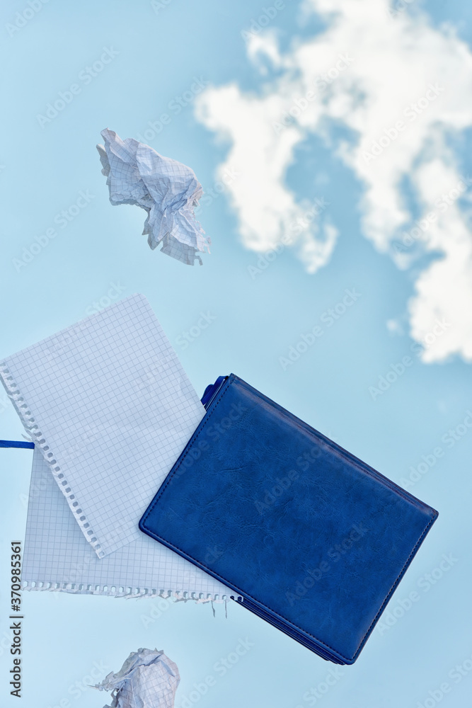 Diary and crumpled sheets of paper in the air against the background of a blue sky with clouds. - obrazy, fototapety, plakaty 