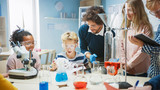 Elementary School Science Classroom: Enthusiastic Teacher Explains Chemistry to Diverse Group of Children, Shows them How to Mix Chemicals in Beakers. Children Use Digital Tablet Computers and Talk