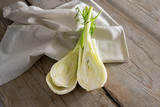 Fresh raw fennel bulb halved, healthy vegetable to cook a Mediterranean summer dish on a napkin and rustic wooden planks, copy space