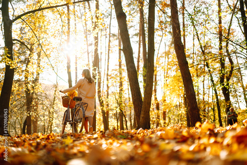 Stylish woman with a bicycle enjoying autumn weather in the park. Beautiful Woman walking  in the autumn forest.