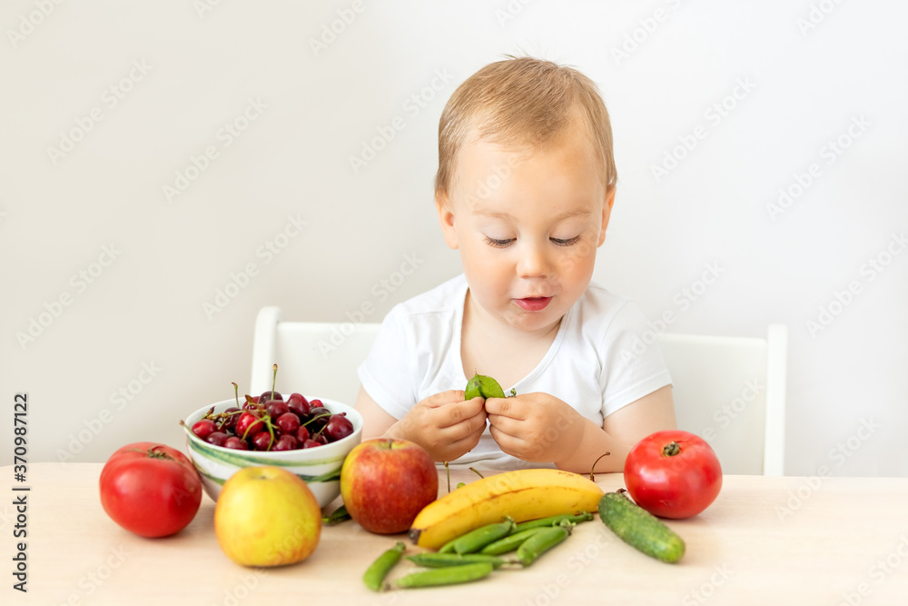 baby boy 2 years old sitting at a table on a white isolated background and eating fruits vegetables, baby food concept, place for text baby boy 2 years old sitting at a table on a white isolated background and eating fruits vegetables, baby food concept, place for text