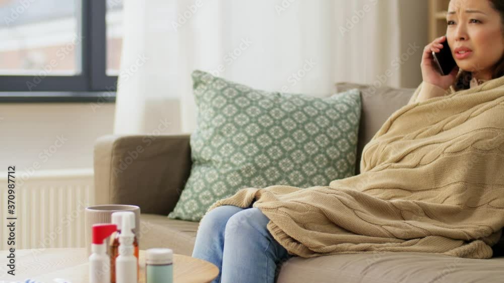 technology, health and cold concept - sick asian woman in blanket calling on smartphone at home technology, health and cold concept - sick asian woman in blanket calling on smartphone at home